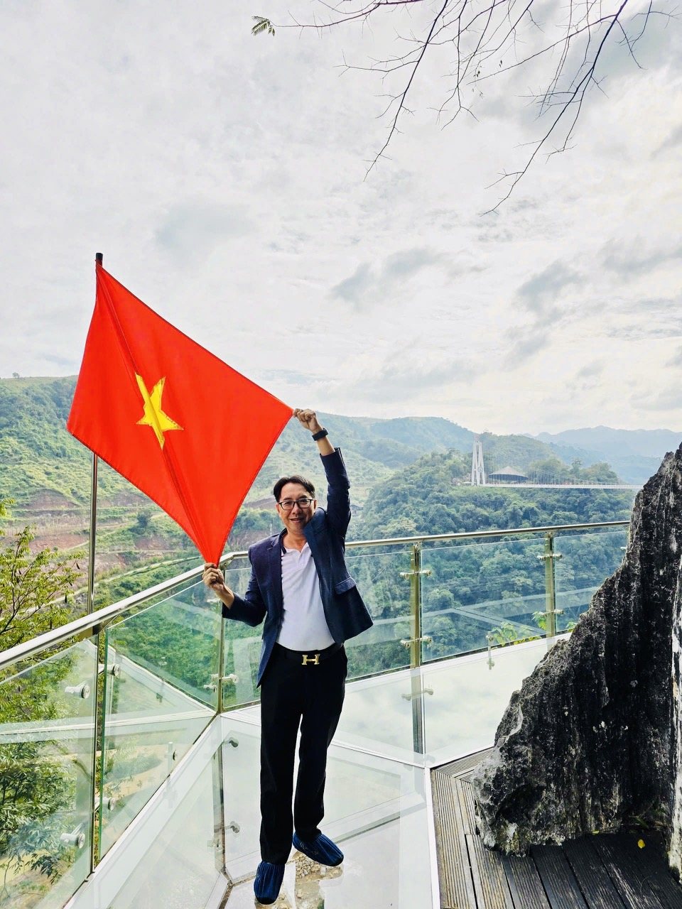 Giang Minh Tuấn cầm cờ đỏ sao vàng trên sàn kính giữa núi rừng Tây Bắc